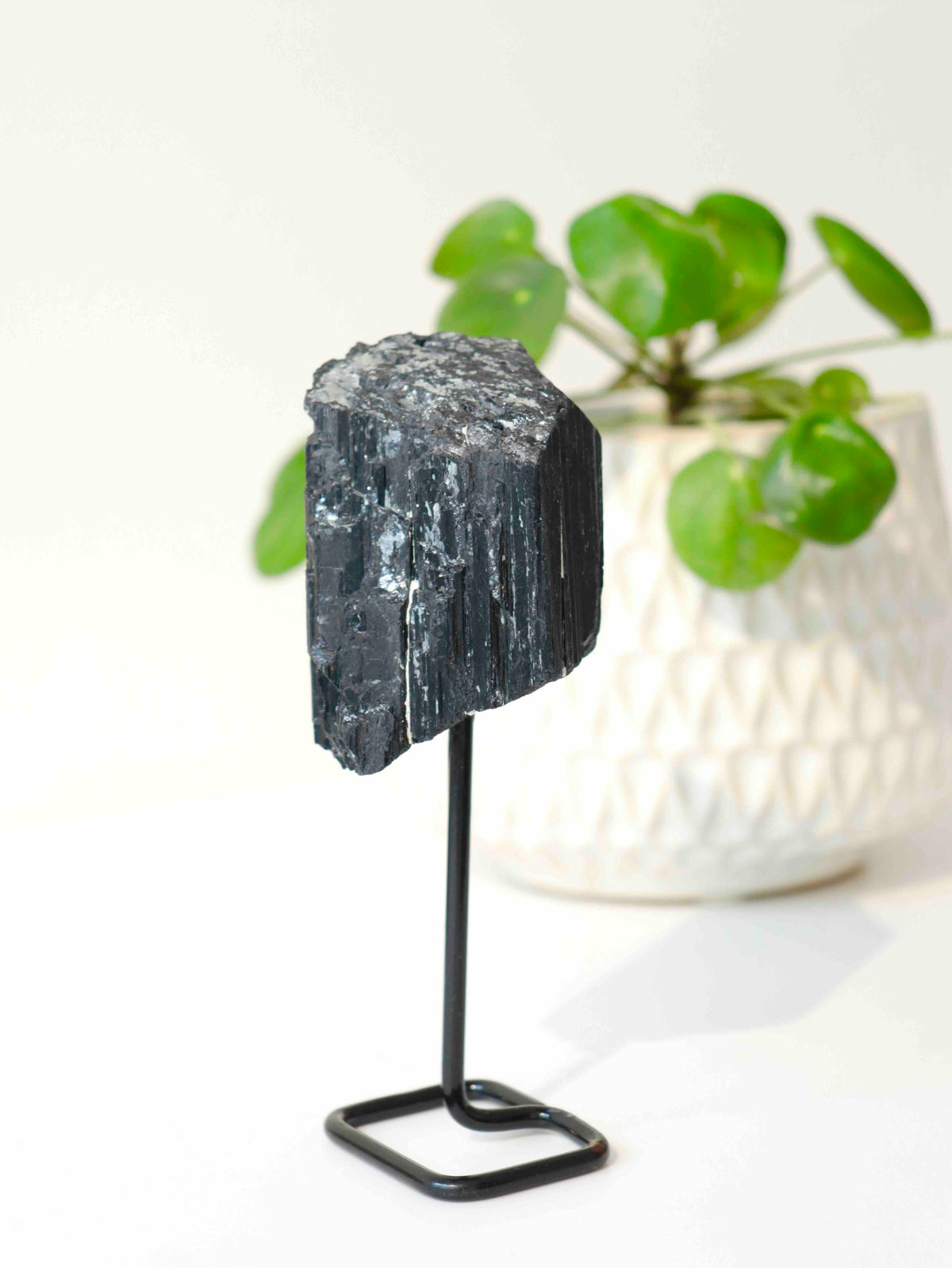Tourmaline noire brute vue sous un autre angle, révélant son sommet rugueux et ses reflets argentés, sur un support métallique noir.
