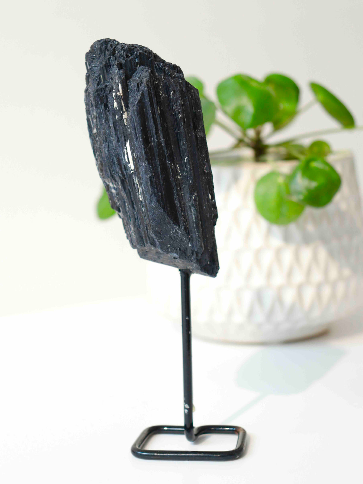 Tourmaline noire brute aux larges faces striées et aux reflets argentés, montée sur un pied métallique noir à base rectangulaire.