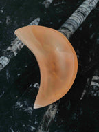 Mini bol lune en sélénite orange aux nuances pêche et aux bords clairs, vu du dessus sur une surface noire à motifs fossiles.
