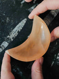 Mini bol en sélénite orange en forme de croissant de lune, tenu entre deux mains, montrant son intérieur creusé et ses reflets satinés.