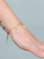  Bracelet en gold-filled 14K porté au poignet, orné de plusieurs charms nuages en quartz rose.