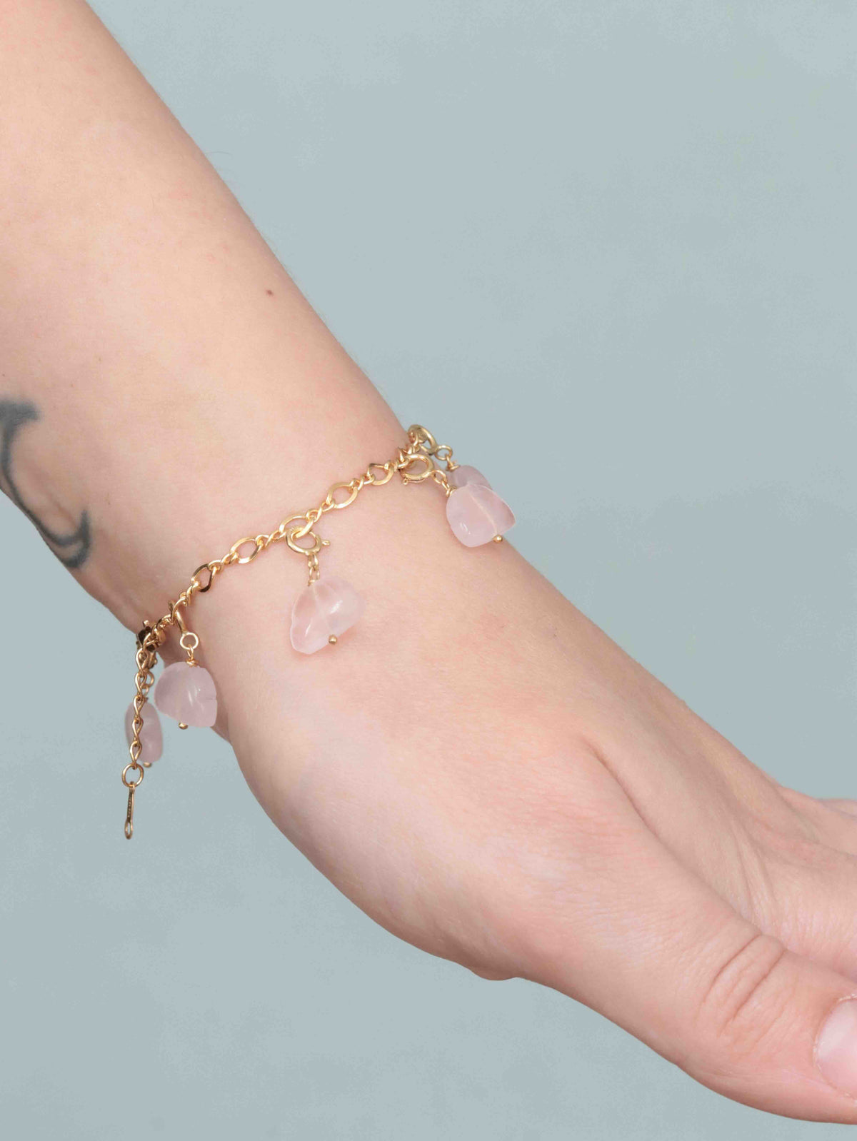  Bracelet en gold-filled 14K porté au poignet, orné de plusieurs charms nuages en quartz rose.