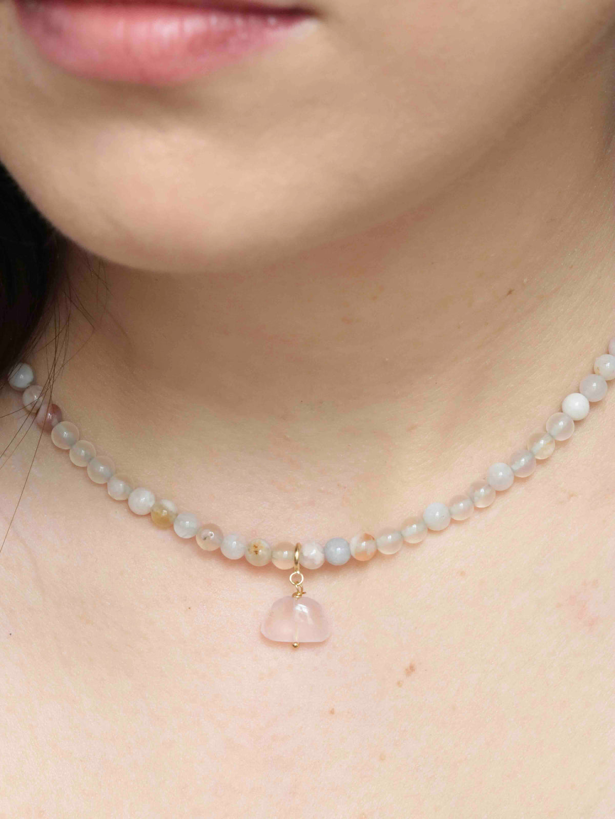 Charm nuage en quartz rose porté en pendentif sur un collier de perles aux teintes pastel.