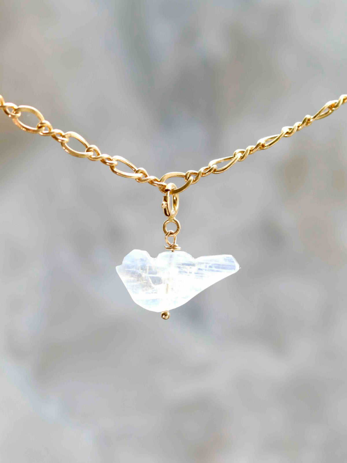 Charm oiseau en pierre de lune blanche aux reflets bleutés, suspendu à une chaîne dorée par un fermoir en gold-filled 14K.