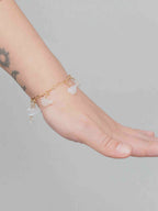 Charm oiseau en pierre de lune porté au poignet sur un bracelet doré, associé à d’autres charms.