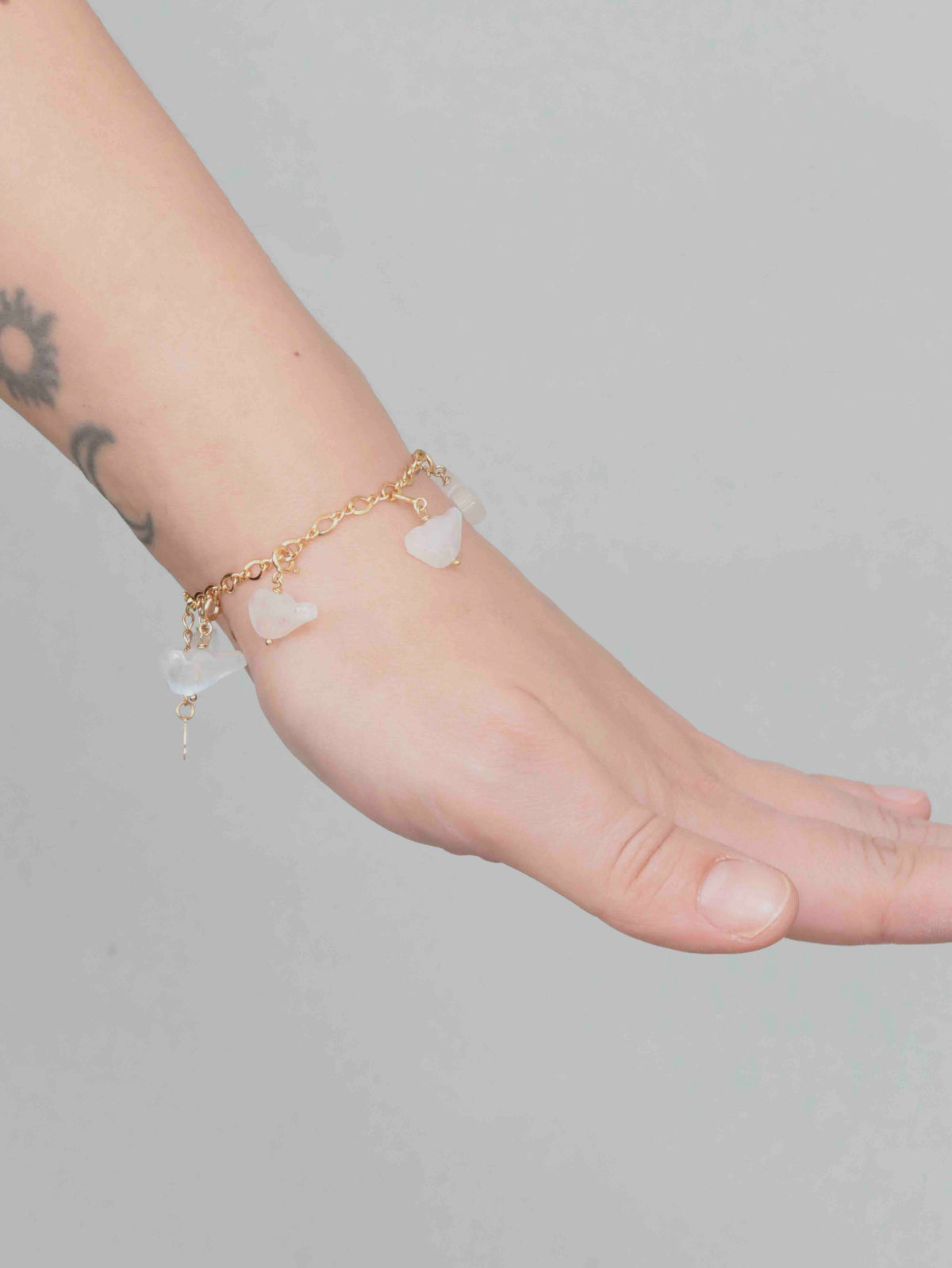 Charm oiseau en pierre de lune porté au poignet sur un bracelet doré, associé à d’autres charms.