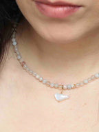 Charm oiseau en pierre de lune avec attache en gold-filled 14K, porté en pendentif sur un collier de perles claires.