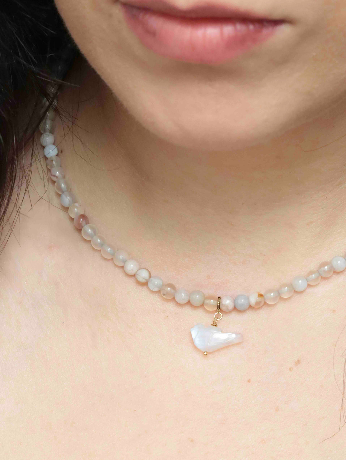 Charm oiseau en pierre de lune avec attache en gold-filled 14K, porté en pendentif sur un collier de perles claires.