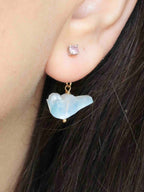 Charm oiseau en pierre de lune aux reflets bleus, porté sous le lobe avec une boucle d’oreille puce.