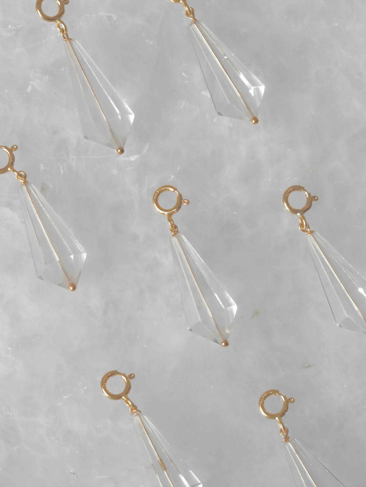 Charms mini Vogel en cristal de roche transparent et Gold-filled 14K disposés sur un fond clair.