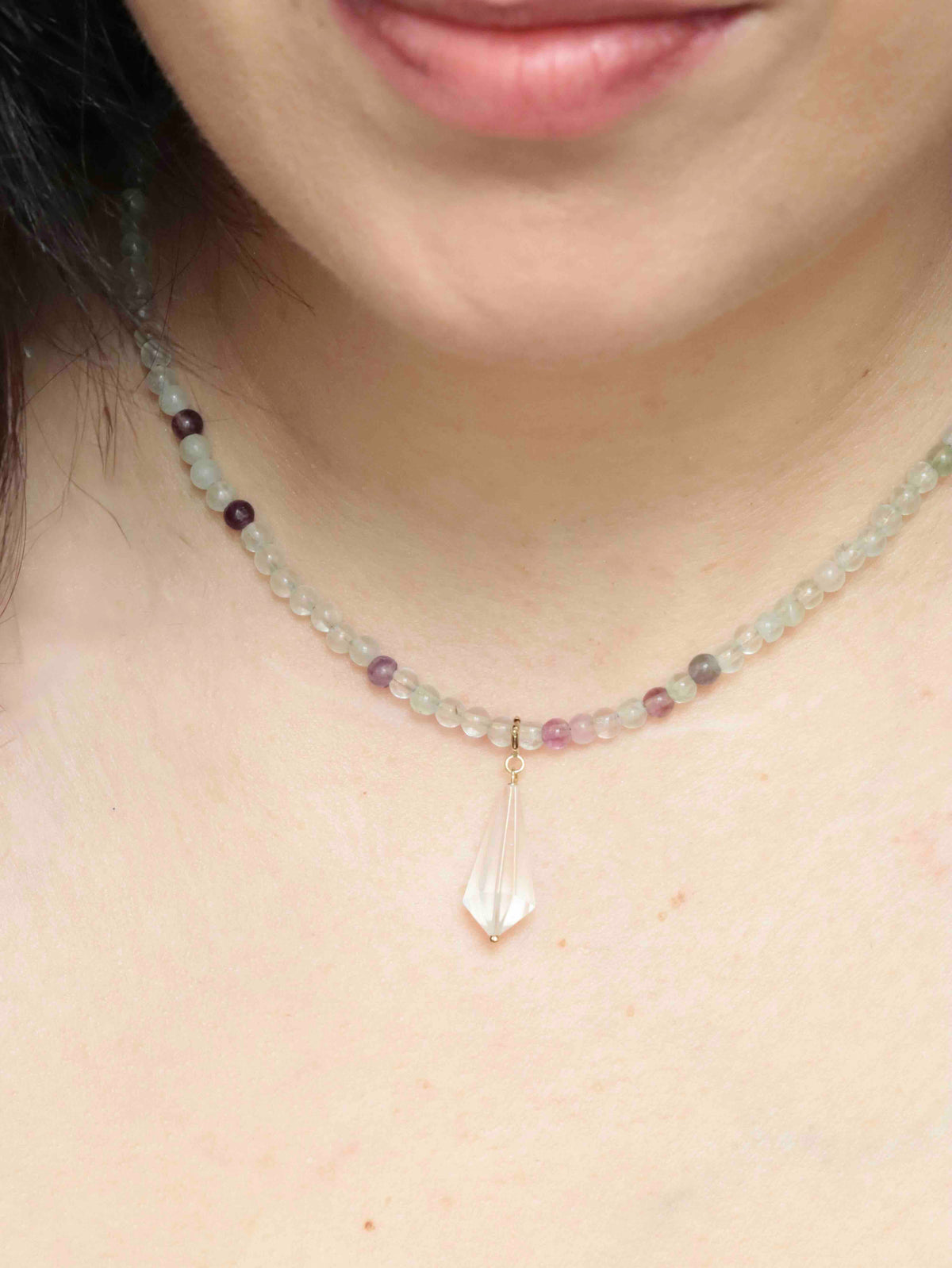 Charm mini Vogel en cristal de roche porté en pendentif sur un collier de perles multicolores.