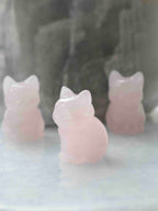 Chat en quartz rose poli vu de trois quarts, avec deux autres figurines de chats en arrière-plan.