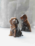 Chien sculpté en œil-de-tigre aux teintes brunes et dorées, vu de face, avec un second chien en arrière-plan.