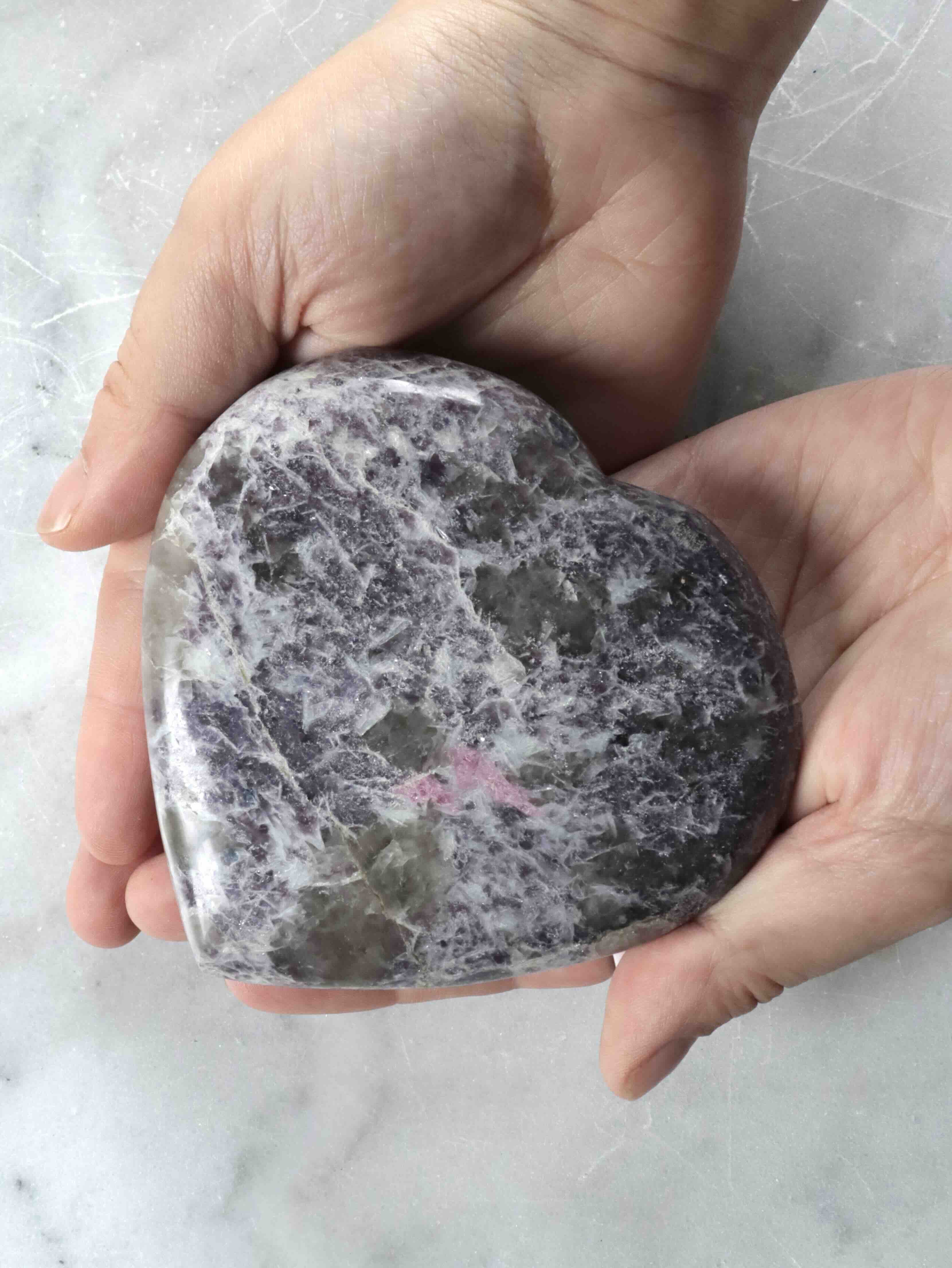 Grand cœur en lépidolite poli tenu en main, inclusions violettes et roses – pierre naturelle pour revenir à l'essentiel – SOLYA Belgique