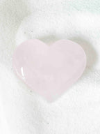 Cœur sculpté en quartz rose naturel, forme lisse et arrondie, posé sur fond blanc texturé