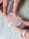 Cœur en quartz rose poli tenu en main, pierre naturelle rose pâle translucide, fond marbre blanc