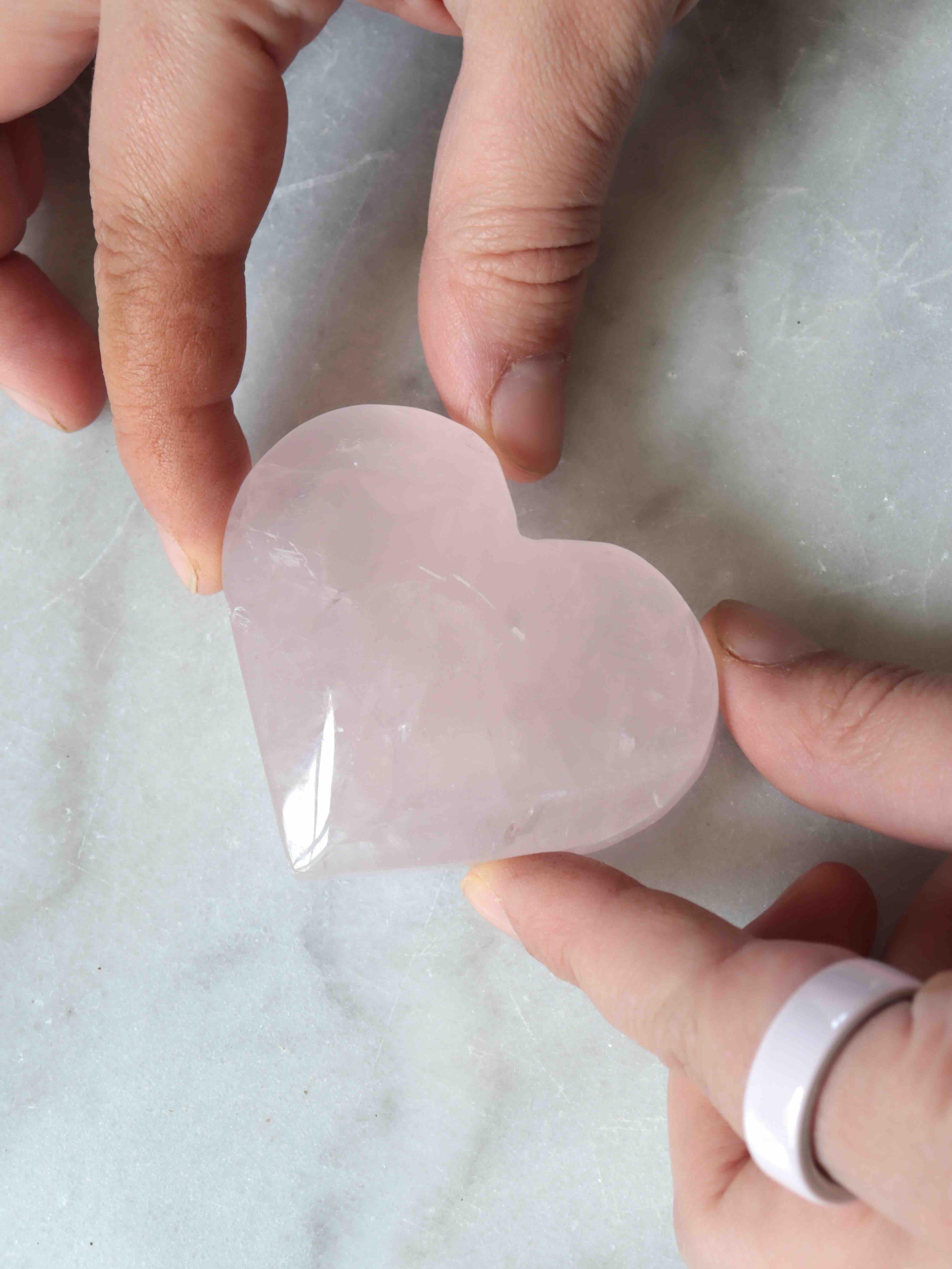 Cœur en quartz rose poli tenu en main, pierre naturelle rose pâle translucide, fond marbre blanc