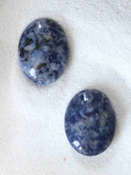 Deux galets de sodalite naturelle polis, teintes bleu nuit et blanc, posés sur fond blanc texturé