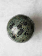 Sphère en jaspe Kambaba sur fond clair, avec de larges motifs noirs dans une pierre vert foncé