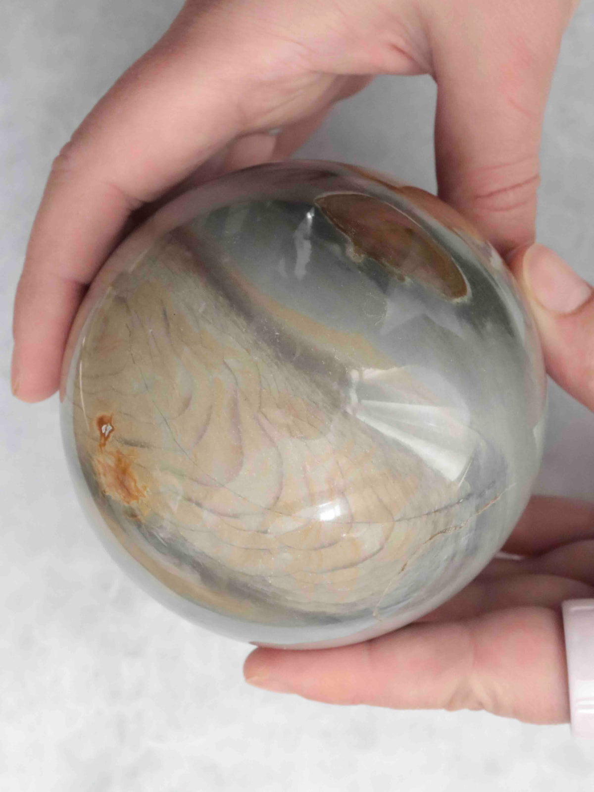 Grande sphère en jaspe polychrome tenue entre deux mains, avec des motifs beige sable et gris-vert.