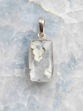 Pendentif rectangulaire en quartz transparent à inclusions de pyrite, serti d’argent 925, vu de face sur un fond minéral clair.