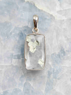 Pendentif rectangulaire en quartz transparent à inclusions de pyrite, serti d’argent 925, vu de face sur un fond minéral clair.