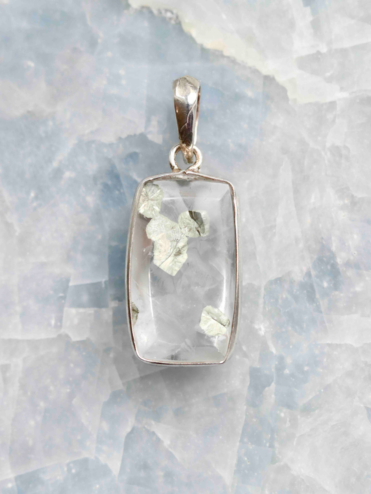 Pendentif rectangulaire en quartz transparent à inclusions de pyrite, serti d’argent 925, vu de face sur un fond minéral clair.