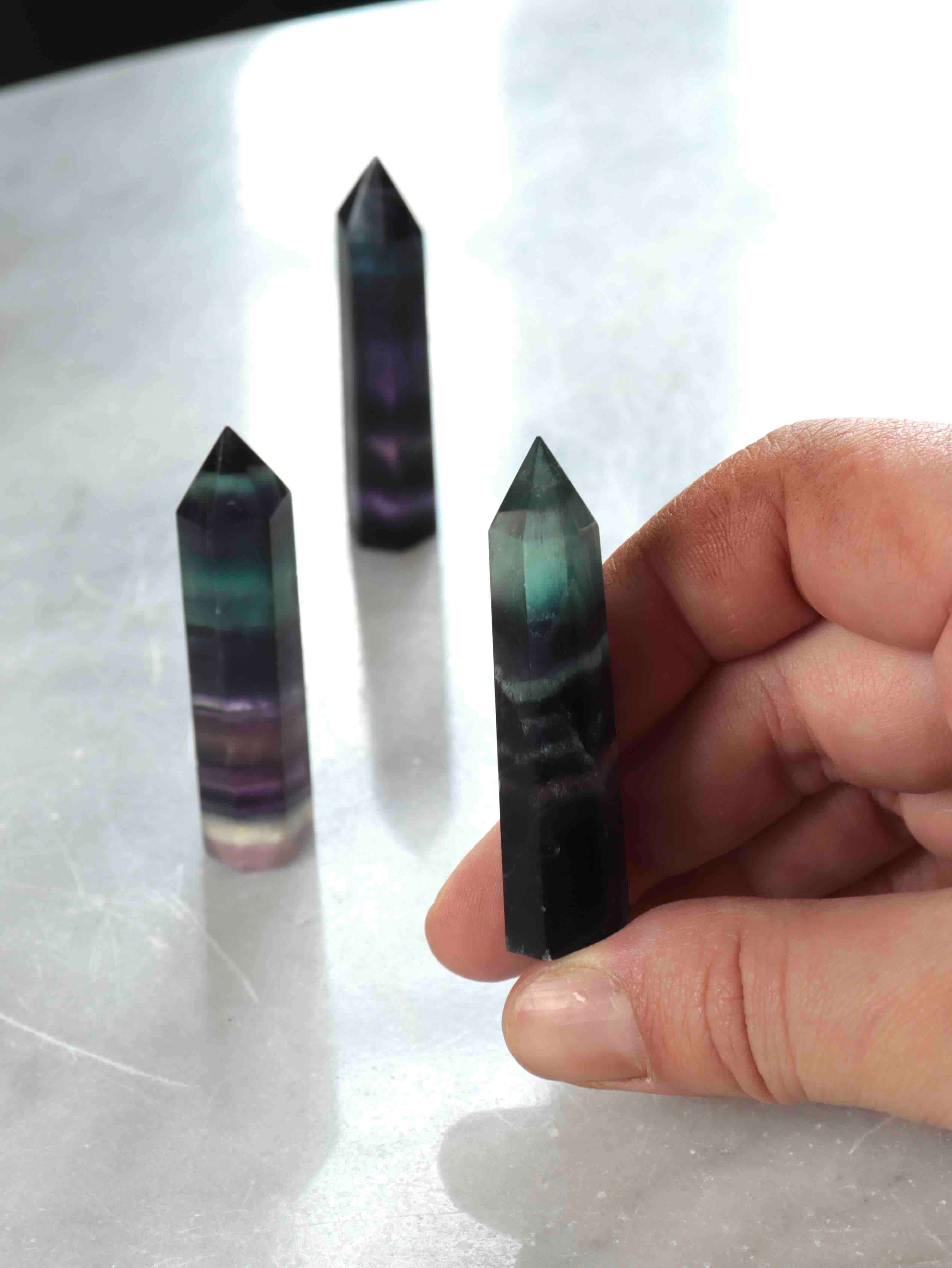 Pointe de fluorite naturelle multicolore vue de côté, bandes vertes et violettes translucides, lumière naturelle