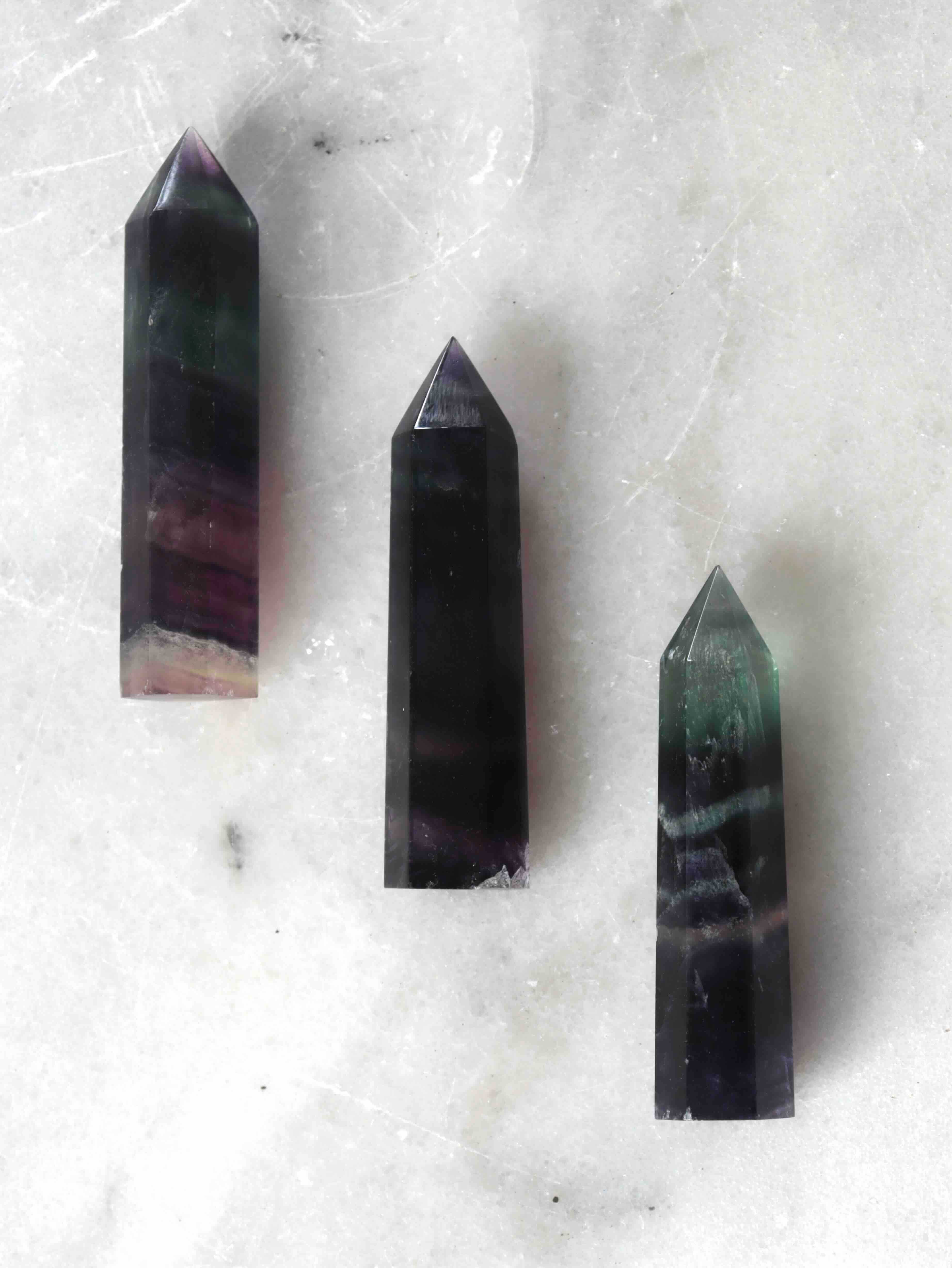 Petite pointe de fluorite multicolore semi-polie, nuances vert menthe et violet, posée sur marbre blanc