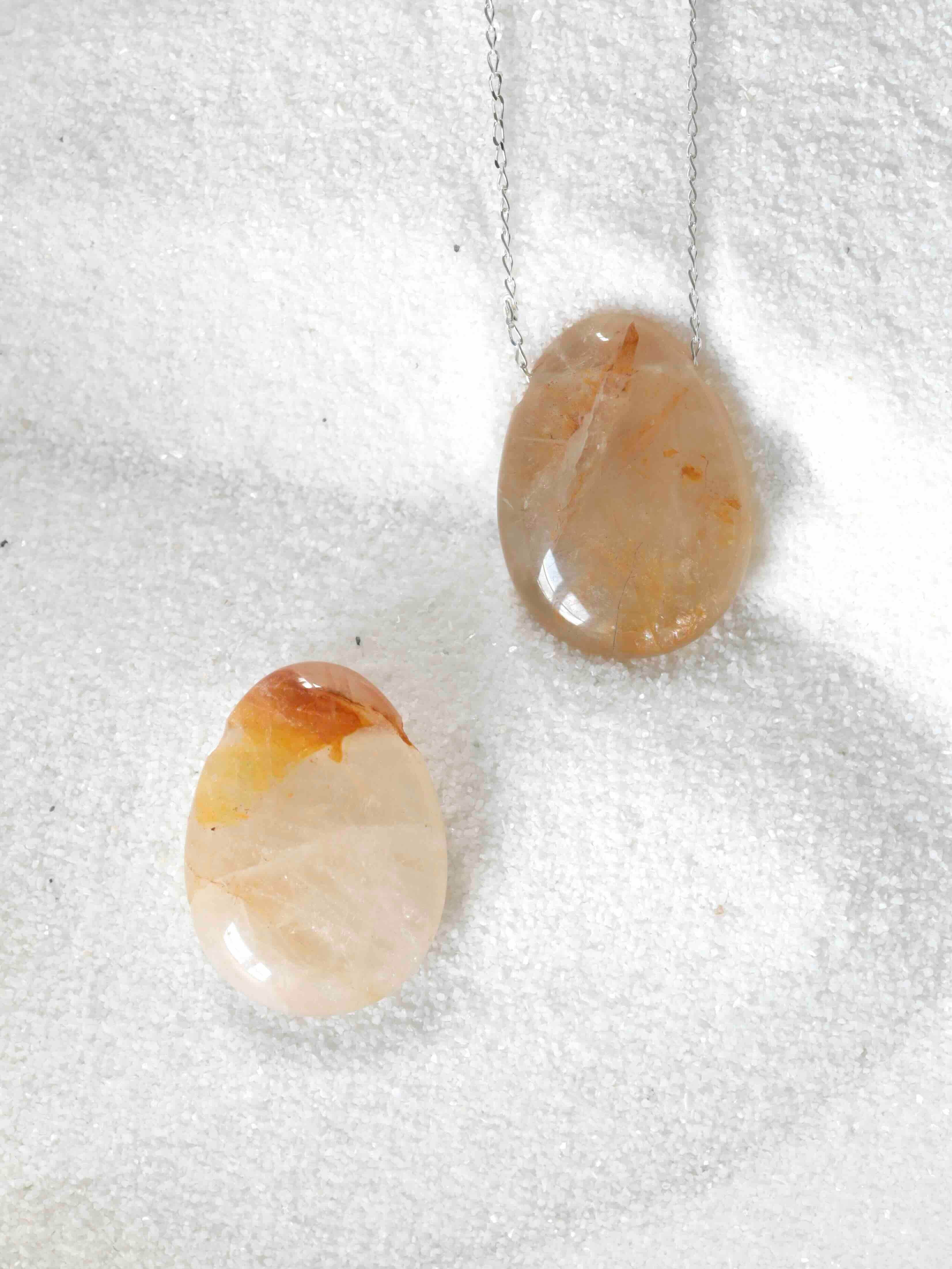 Deux gemmes percées en quartz doré naturel, teintes miel et blanc nacré, l'une sur chaîne argentée, fond blanc texturé