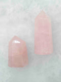 Deux pointes polies en quartz rose de tailles différentes, aux nuances rose pâle et aux veinures blanchâtres, sur fond clair.