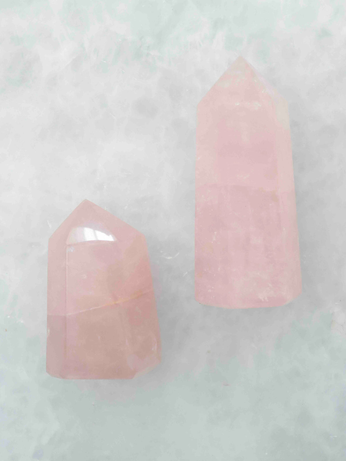 Deux pointes polies en quartz rose de tailles différentes, aux nuances rose pâle et aux veinures blanchâtres, sur fond clair.