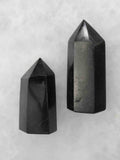 Deux pointes polies en tourmaline noire de tailles différentes, aux facettes brillantes et aux fines veinures, sur fond clair.
