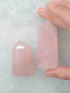 Grande pointe en quartz rose tenue entre les doigts à côté d’une pointe plus petite, montrant leurs facettes polies.