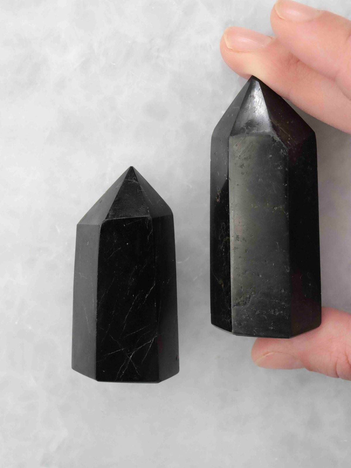 Grande pointe en tourmaline noire tenue entre les doigts à côté d’une pointe plus petite, montrant leurs facettes polies.