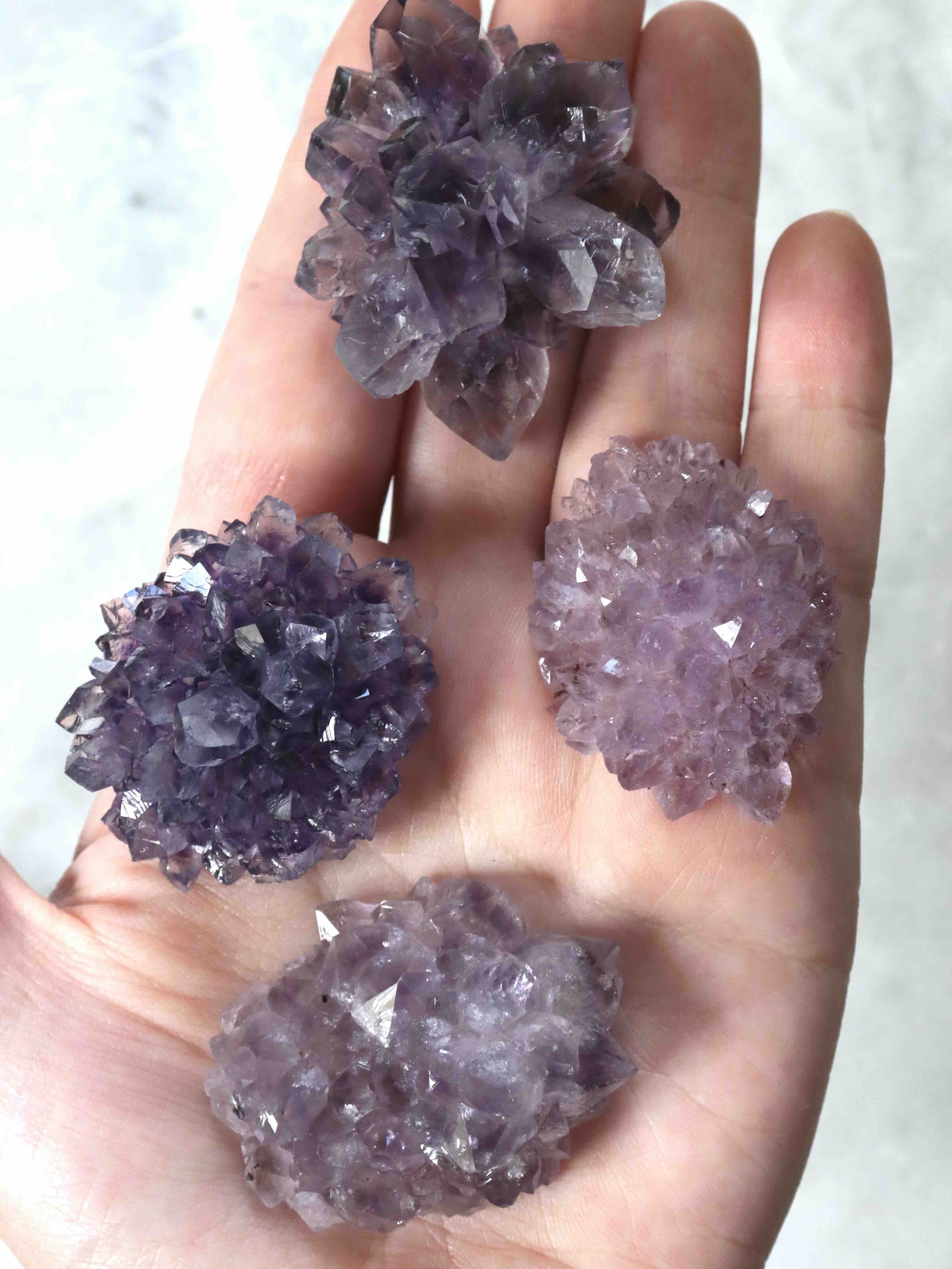 Petites fleurs d'améthyste naturelles posées sur fond neutre, reflets mauves lumineux, pièces de collection uniques