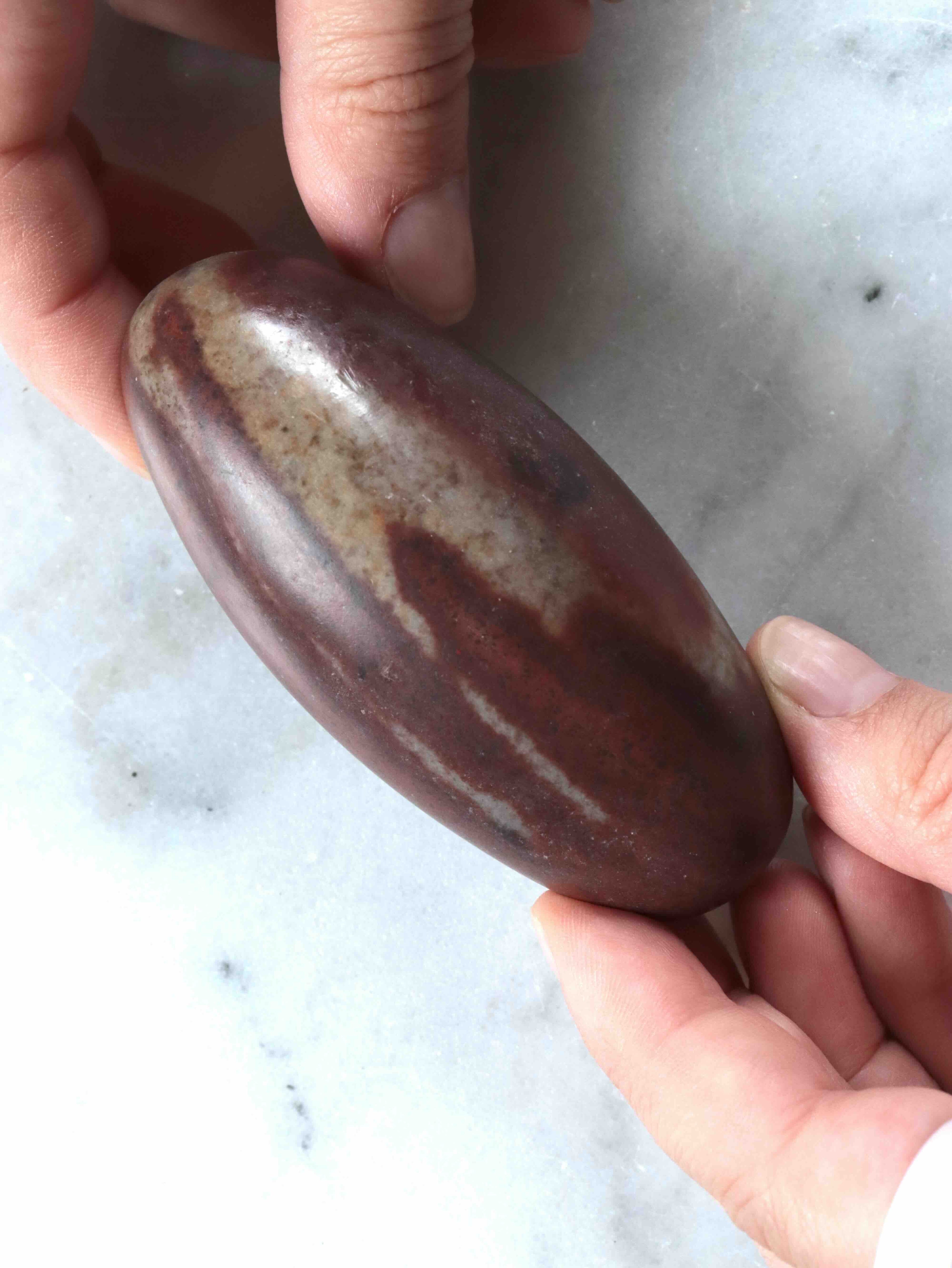 Shiva Lingam tenu en main, bandes beiges caractéristiques – taille réelle, pierre éthique – SOLYA
