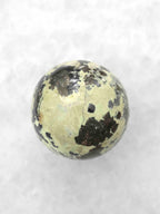 Sphère en serpentine vue sous un autre angle, avec une large zone vert clair, de fines veinules et des taches noires.