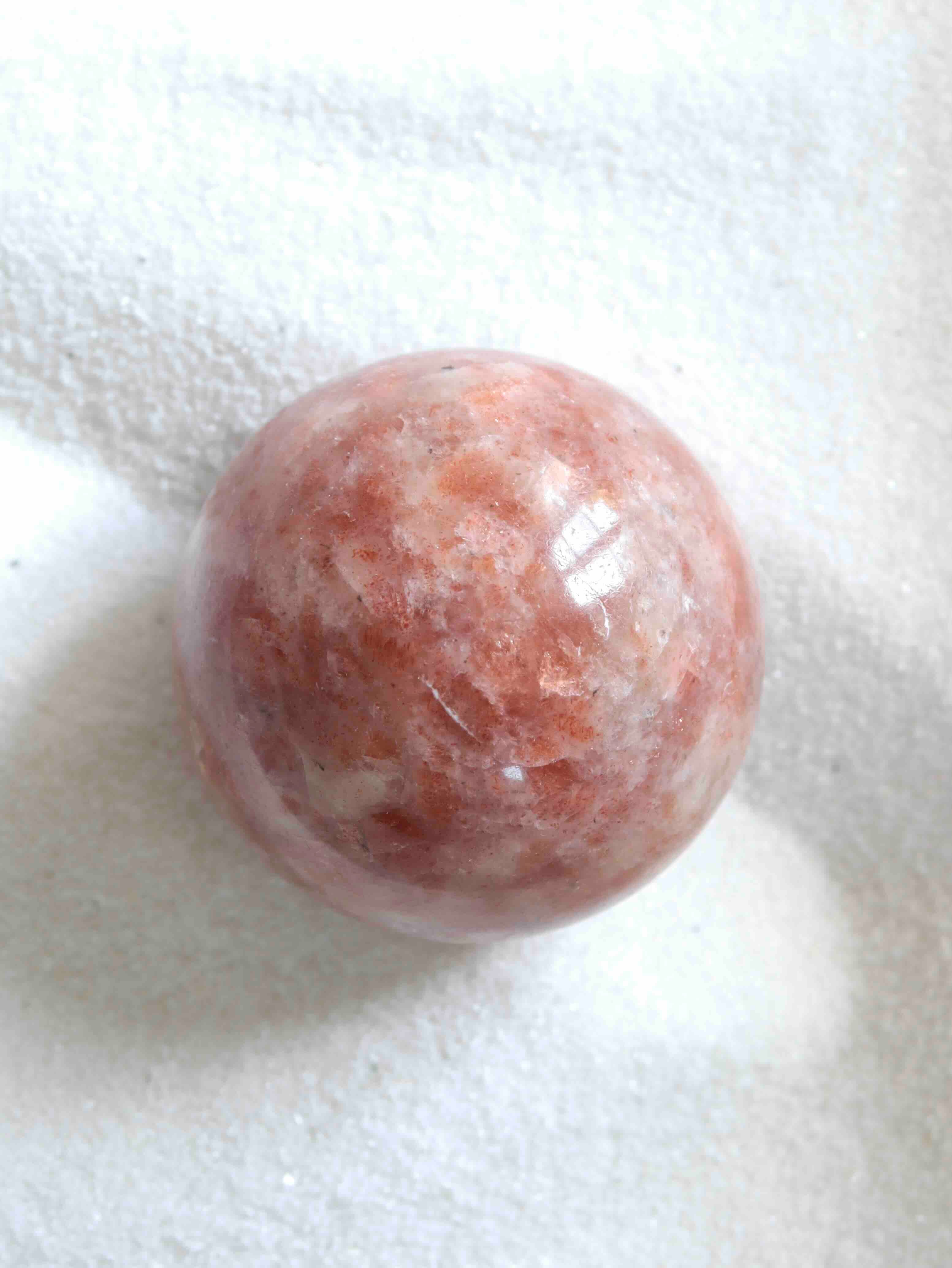 Sphère de pierre de soleil naturelle, reflets dorés et inclusions scintillantes, posée sur fond blanc texturé