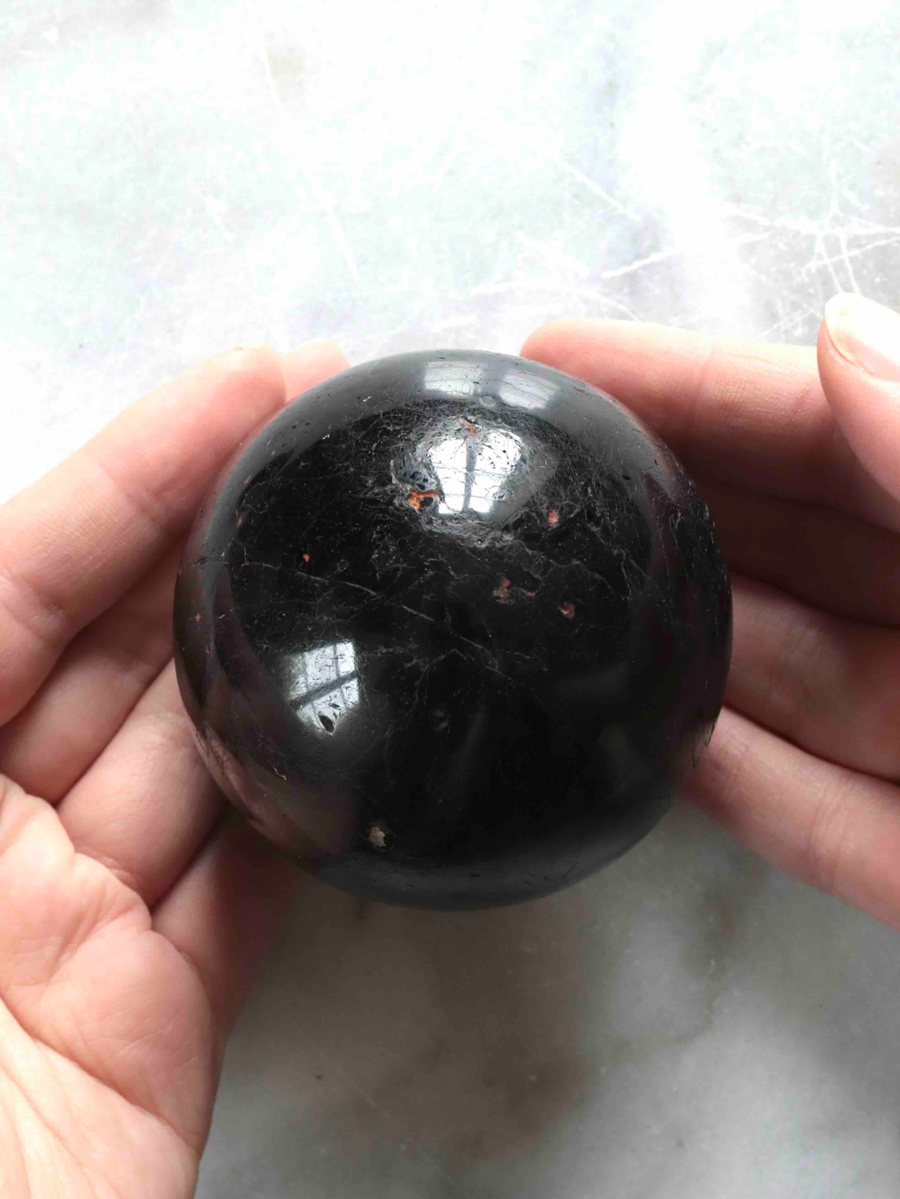 Sphère en tourmaline noire du Brésil tenue dans les mains – pierre naturelle polie pour éloigner les énergies négatives – SOLYA Belgique